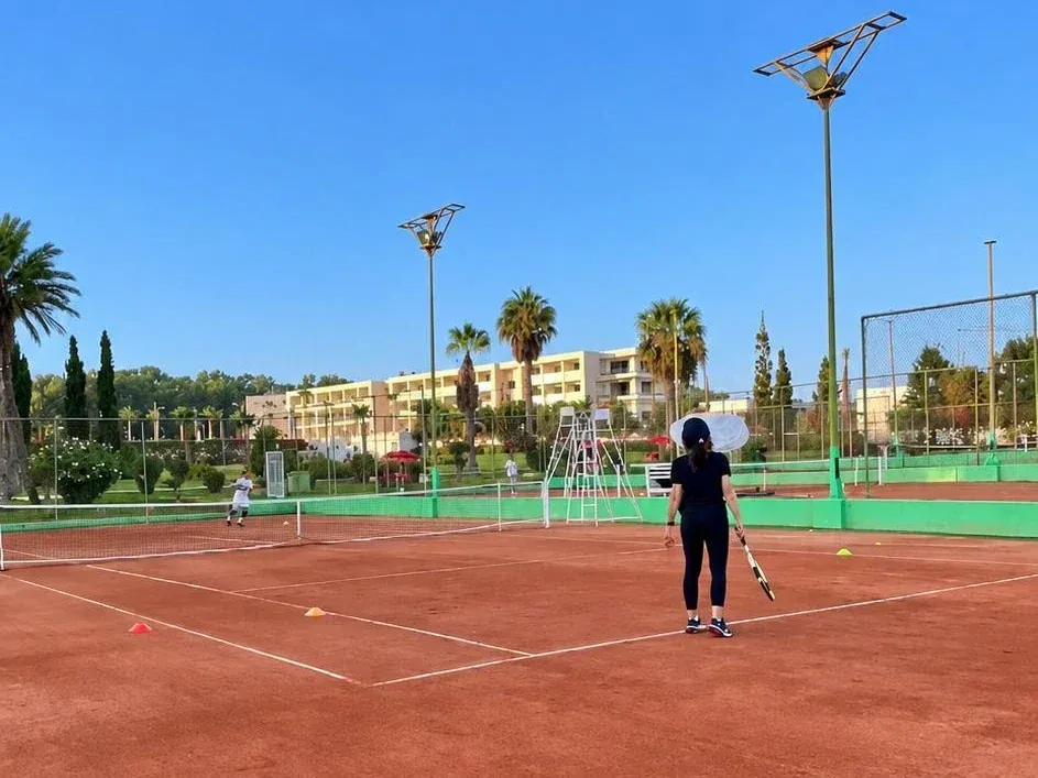 Location de terrain de tennis à Agadir : courts en terre battue du club en plein jour, entourés de palmiers et de projecteurs