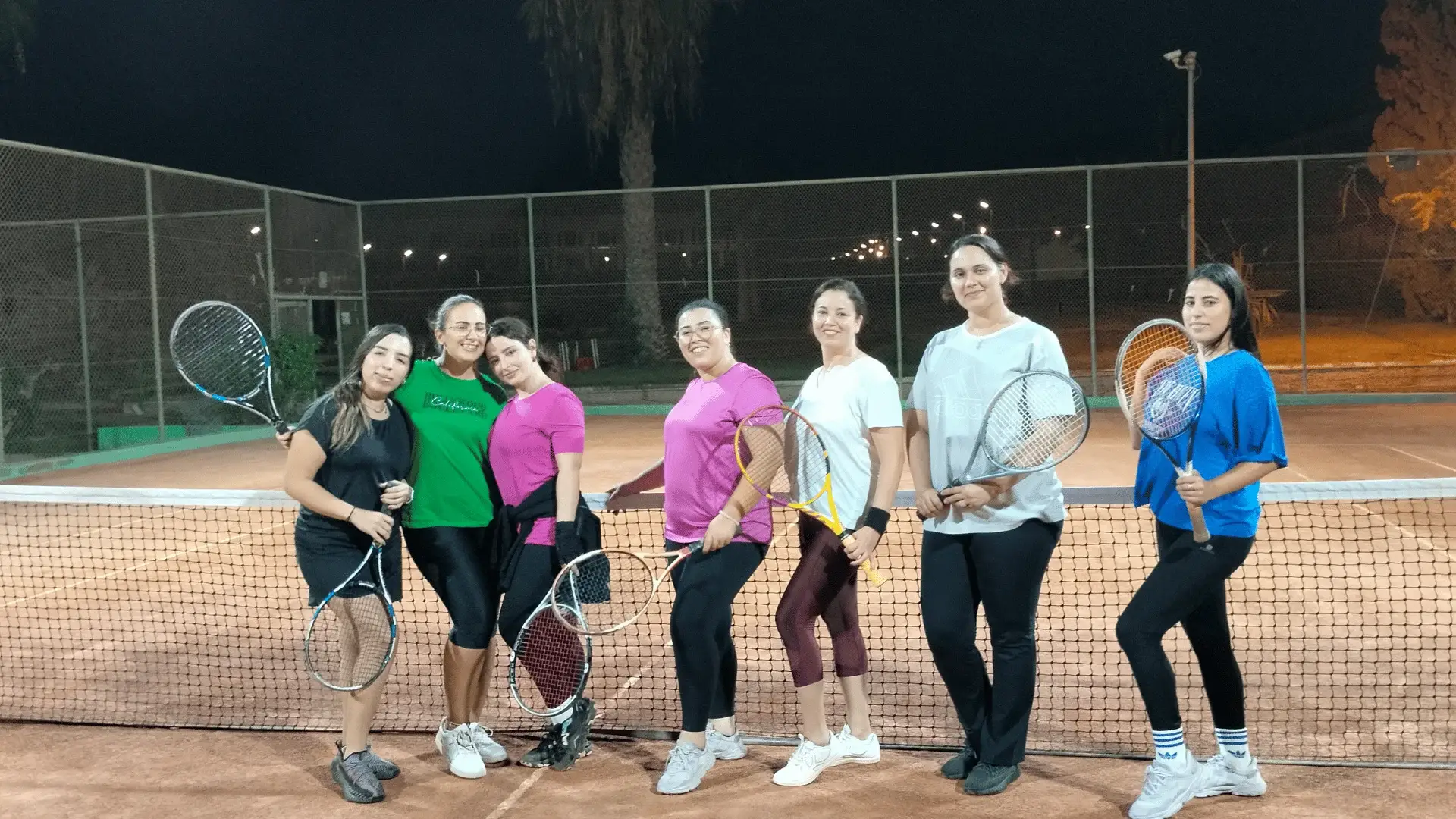 Les joueuses de l’école de tennis 100 % femmes rassemblées au filet, le soir sous les projecteurs du club